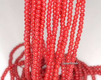 May include: A strand of bright red coral beads. The beads are round and smooth, and they are strung on a clear thread. The beads are all the same size, and they are arranged in a neat, even row. The beads are a beautiful shade of red, and they have a natural, organic look.