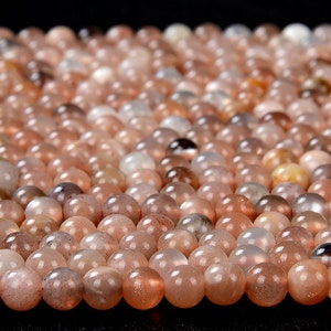 May include: A close-up of a pile of round, smooth, light brown sunstone beads. The beads have a shimmery, iridescent quality.