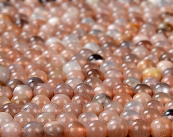 May include: A close-up of a pile of round, smooth, light brown sunstone beads. The beads have a shimmery, iridescent quality.