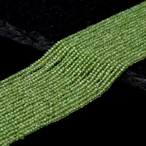 May include: A strand of green peridot beads, faceted and round, arranged in rows on a black surface.