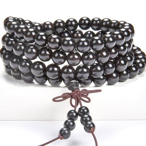 May include: A black wooden beaded necklace with a brown cord tassel. The beads are round and smooth, and the necklace is strung on a single cord.