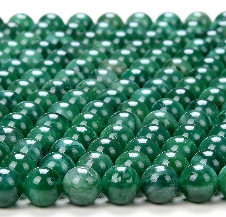 May include: A close-up view of a collection of round, green jade beads. The beads are smooth and polished, with a slight variation in color and pattern.