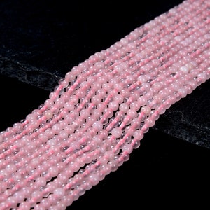 May include: A strand of pink rose quartz beads. The beads are round and smooth, and they have a translucent appearance. The beads are strung on a clear thread.