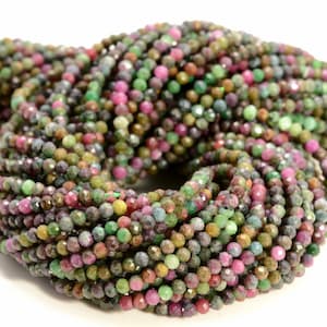 May include: A strand of faceted gemstone beads in shades of green, pink, and purple. The beads are small and round, and they are strung together on a clear thread.