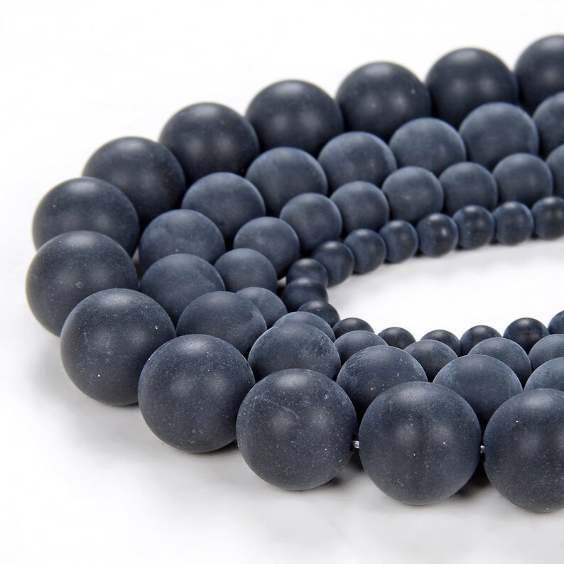 May include: A strand of black matte round beads of varying sizes. The beads are arranged in a semi-circle, with the largest beads at the top and the smallest beads at the bottom.