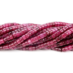 Op de afbeelding: Een streng roze robijn edelsteen kralen, elke kraal is vierkant met afgeronde randen.