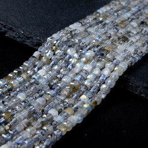 May include: A strand of faceted, iridescent labradorite beads in shades of gray and blue. The beads are rectangular in shape and have a smooth, polished finish.