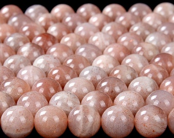 May include: A close-up of a group of round, smooth, sunstone beads. The beads are a light peach color with a slight shimmer.