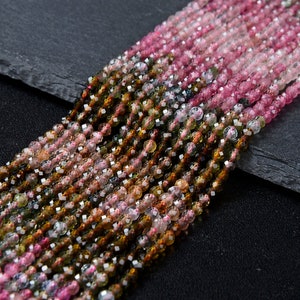Könnte beinhalten: Eine Strähne aus mehrfarbigen Edelsteinperlen. Die Perlen sind facettiert und haben eine Vielzahl von Farben, darunter Rosa, Grün und Braun. Die Perlen sind auf einem durchsichtigen Faden aufgefädelt.