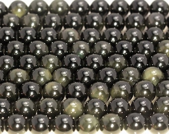 May include: A close-up of a collection of black obsidian beads with a green iridescent sheen. The beads are round and smooth, and they are arranged in a staggered pattern.