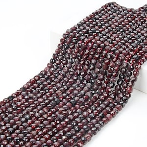 May include: A strand of dark red faceted garnet beads. The beads are round and have a smooth, polished finish.
