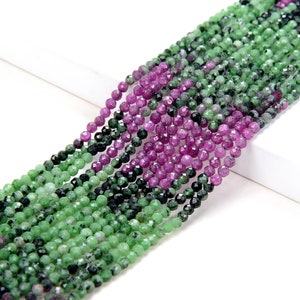 Peut inclure: Un brin de perles de pierres précieuses facettées vertes et roses. Les perles sont petites et rondes, et elles sont enfilées sur un fil transparent. Les perles sont disposées en un motif dégradé, avec les perles vertes en bas et les perles roses en haut.
