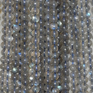 May include: Strands of round, translucent beads with a gray and blue iridescence. The beads are strung together with a blue cord, creating a vertical pattern. The beads are approximately 0.8 cm in diameter.