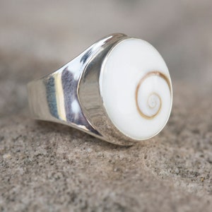 May include: A silver ring with a white shell inlay featuring a spiral pattern.