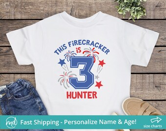 May include: White t-shirt with a blue and red graphic that says "This Firecracker is 3 Hunter". The graphic features a large blue number 3 with red and white fireworks around it.