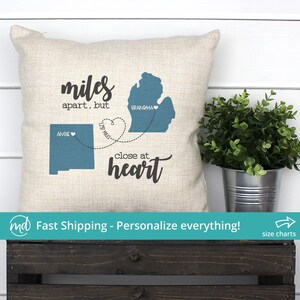 May include: A beige throw pillow with a blue outline of Michigan and New Mexico with the text "miles apart, but close at heart" and the names "Grandma" and "Angie" on each state.