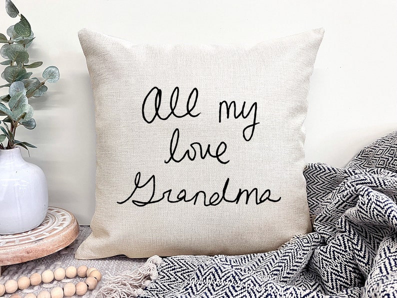 May include: A beige throw pillow with black cursive text that reads "all my love Grandma".