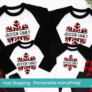 May include: A set of four matching pajamas featuring a red and black plaid pattern with a white snowflake design. The snowflake has a black border and the text "JACKSON FAMILY" written across it.