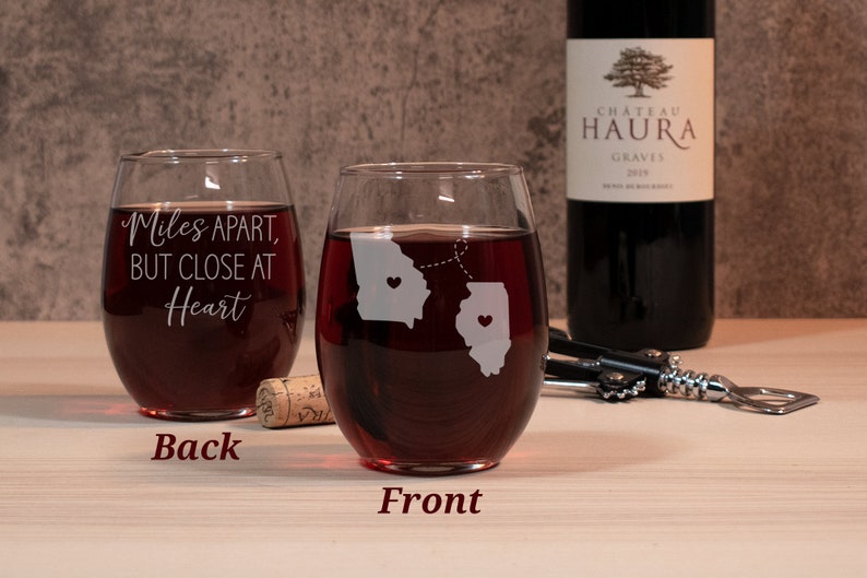 May include: Two stemless wine glasses with a design of the states of Georgia and Illinois with hearts in each state and a dotted line connecting them. The text on the back of one glass reads "Miles Apart, But Close At Heart".
