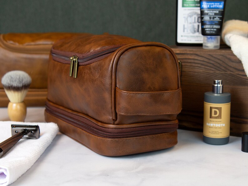 May include: A brown leather travel toiletry bag with two zippered compartments. The bag has a gold zipper and a brown leather handle.