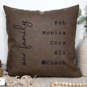 May include: A brown throw pillow with the text "our family" on the left side and the names "Rob", "Monica", "Cora", "Eli", and "Coach" with a paw print on the right side.