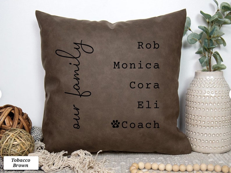 May include: A brown throw pillow with the text "our family" on the left side and the names "Rob", "Monica", "Cora", "Eli", and "Coach" with a paw print on the right side.