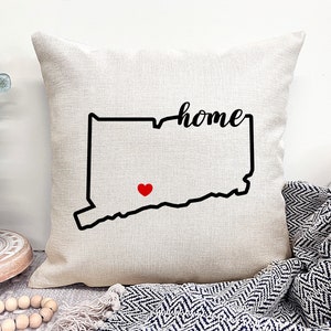 May include: A white throw pillow with a black outline of the state of Connecticut and the word "home" written in cursive. A red heart is placed in the center of the state.