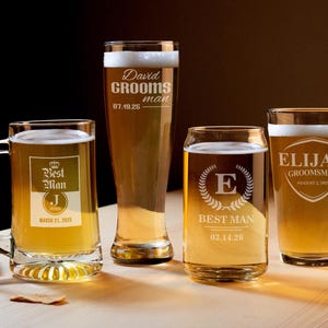 May include: Four personalized beer glasses filled with beer. The glasses include a mug, a tall pilsner, a can-shaped glass, and a pint glass. Each glass is engraved with text such as "Best Man" and names with dates. The glasses are on a light-colored wooden surface.