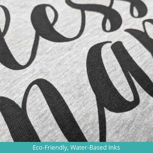 May include: Close-up of a gray sweatshirt with the word "bless" printed in black, using eco-friendly, water-based inks.