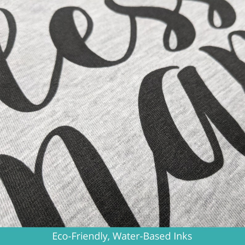 May include: Close-up of a gray sweatshirt with the word "bless" printed in black, using eco-friendly, water-based inks.