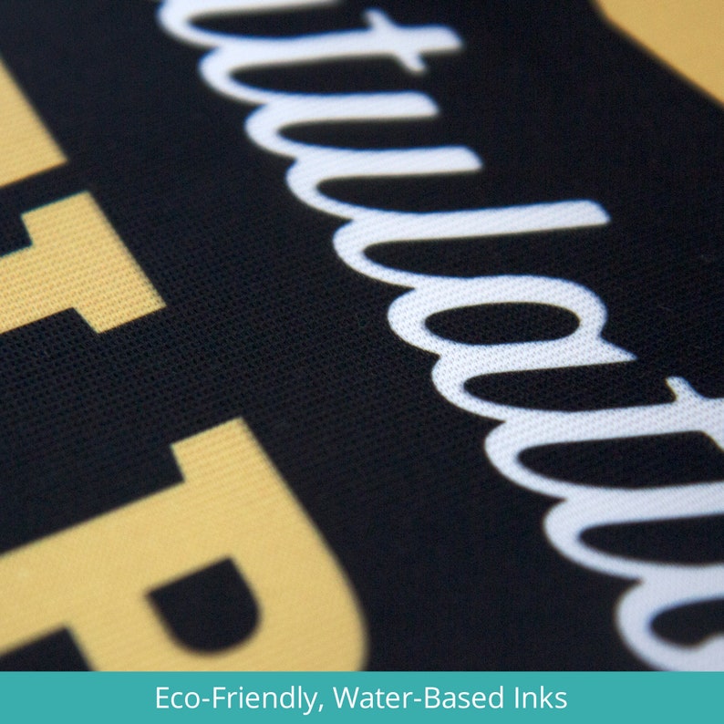 May include: Close-up of a black fabric with the word "attitude" printed in white. The fabric has a textured surface and is made with eco-friendly, water-based inks.