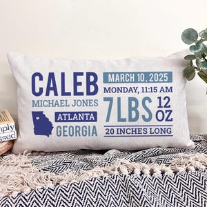 May include: A white pillow with blue and gray text and a blue outline of the state of Georgia with a heart in the center. The text reads "Caleb, Michael Jones, Atlanta, Georgia, March 10, 2025, Monday, 11:15 AM, 7 lbs 12 oz, 20 inches long".