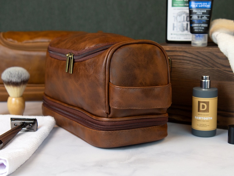 May include: A brown leather travel toiletry bag with two zippered compartments. The bag has a gold zipper and a brown leather handle.