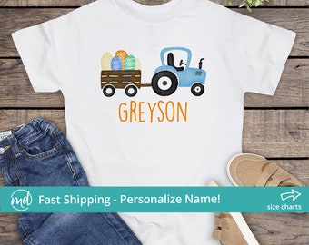 May include: White t-shirt with a blue tractor pulling a wagon full of colorful Easter eggs. The text "GREYSON" is printed in orange below the tractor.