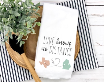 May include: White kitchen towel with the text "Love knows no distance" and a heart with a dotted line connecting two states, Texas and Michigan. 