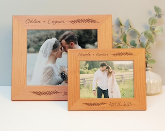 May include: Two wooden picture frames with engraved names and dates. The top frame has the names "Chloe + Logan" and a leafy design. The bottom frame has the names "Nicole + Kevin" and the date "April 20, 2025".