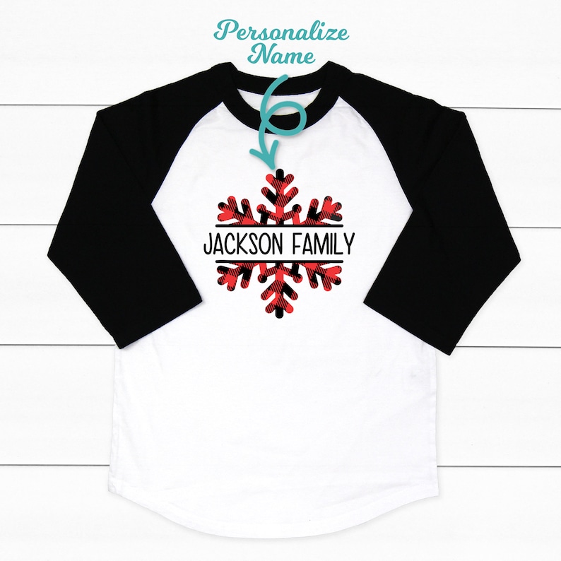 May include: White and black baseball tee shirt with red and black buffalo plaid snowflake design. The text "JACKSON FAMILY" is centered on the snowflake.