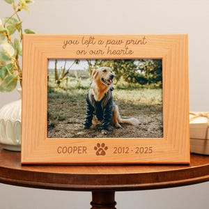 May include: A wooden photo frame with a picture of a golden retriever in a field. The frame has the text "You left a paw print on our hearts" and "COOPER 2012-2025" engraved on it.