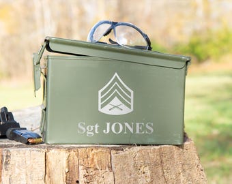 May include: Green metal ammo can with a white Sergeant rank insignia and the name "Sgt JONES" printed on the front. The can is open and has safety glasses on top.