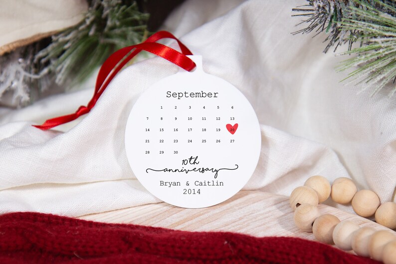 May include: White round ornament with a calendar for September with a red heart on the 25th. The text reads "10th anniversary Bryan & Caitlin 2014".