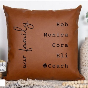 May include: A brown leather cushion with the text "our family" and the names Rob, Monica, Cora, Eli, and Coach printed on it.