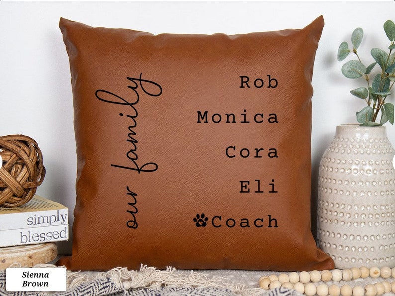 May include: A brown leather cushion with the text "our family" and the names Rob, Monica, Cora, Eli, and Coach printed on it.