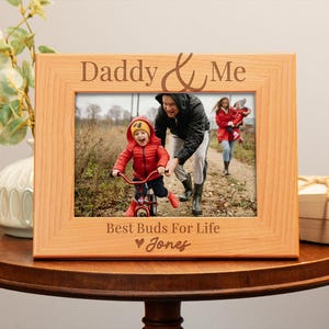 May include: A wooden photo frame with the text "Daddy & Me" and "Best Buds For Life" with a heart and the name "Jones". The frame has a photo of a father and son in a park.