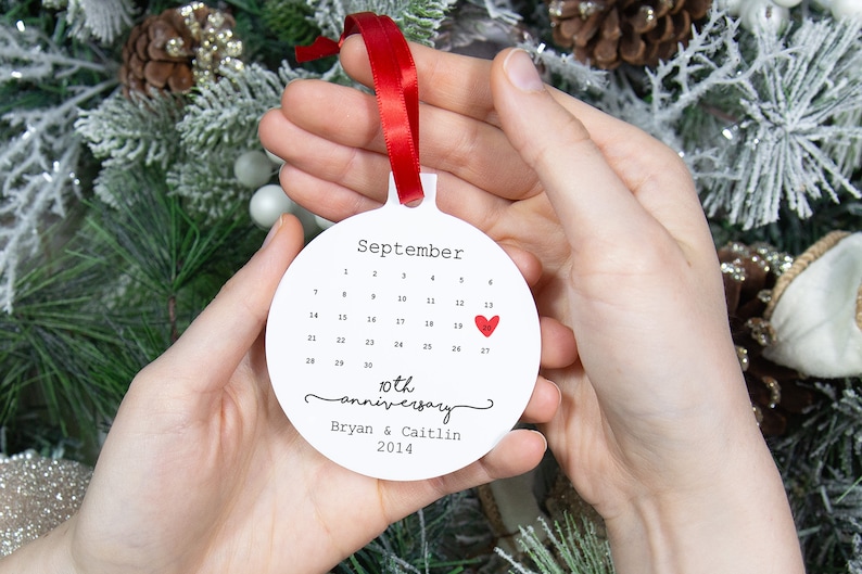 May include: White round ornament with a calendar for September with a red heart on the 13th. The ornament says "10th anniversary Bryan & Caitlin 2014".