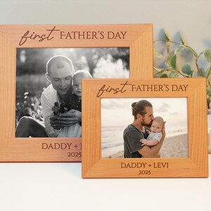 May include: Two light brown wooden photo frames. Each frame has a photograph of a father and child. The frames are inscribed with "first FATHER'S DAY" and "DADDY + [child's name] 2025". The frames are of different sizes.