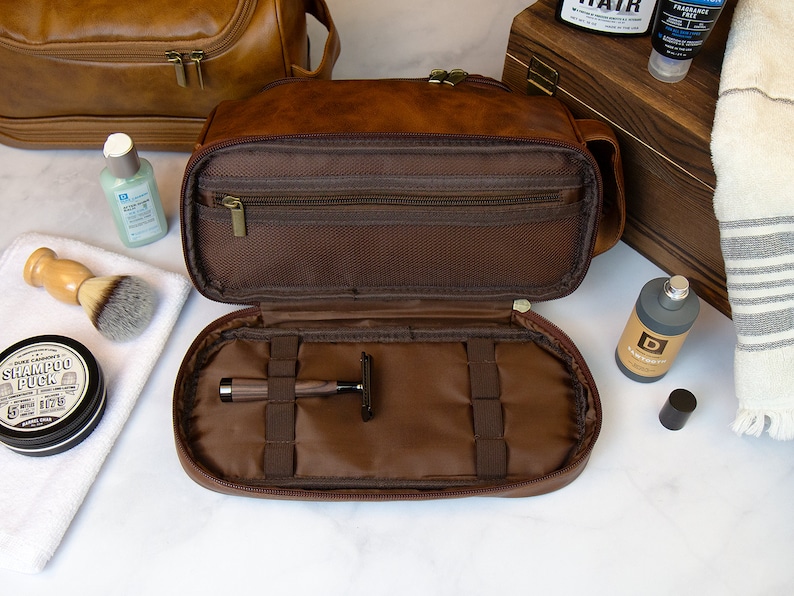 May include: A brown leather travel toiletry bag with a zippered top and multiple compartments. The bag is open and shows a razor and other compartments.