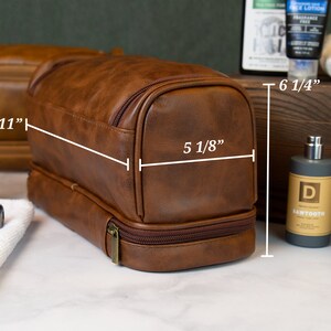 May include: Brown leather travel toiletry bag with two compartments and a zipper closure. The bag measures 11 inches long, 6 1/4 inches tall, and 5 1/8 inches wide.