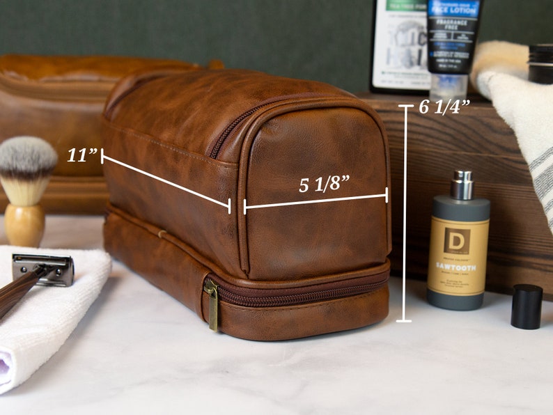 May include: Brown leather travel toiletry bag with two compartments and a zipper closure. The bag measures 11 inches long, 6 1/4 inches tall, and 5 1/8 inches wide.