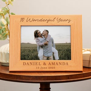 May include: A wooden photo frame with a light brown finish. The frame has a photo of a couple smiling and holding each other. The text "10 Wonderful Years" is engraved on the top of the frame. The text "Daniel & Amanda" and "13 June 2025" is engraved on the bottom of the frame.