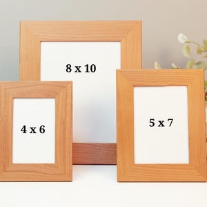 May include: Three wooden picture frames in varying sizes: 4 x 6 inches, 5 x 7 inches, and 8 x 10 inches. The frames are a light brown colour with white matting. The frames are displayed on a white surface.